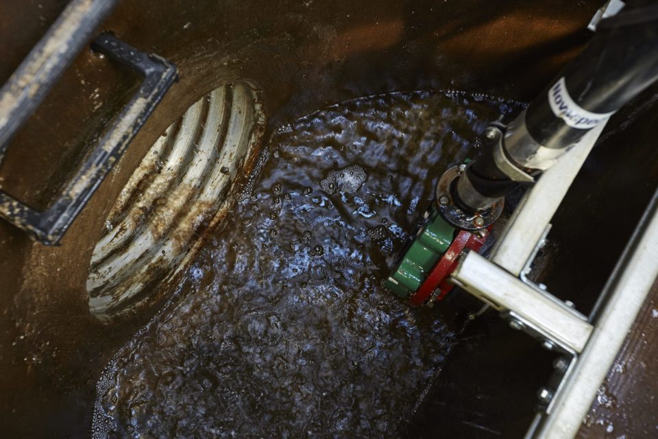 A corrugated metal pipe drains water from the pond, with valves and pipes of the automated system above the water. 