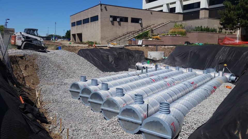 A large hole in front of the school's entrance with several corrugated metal pipes laying in gravel during construction.