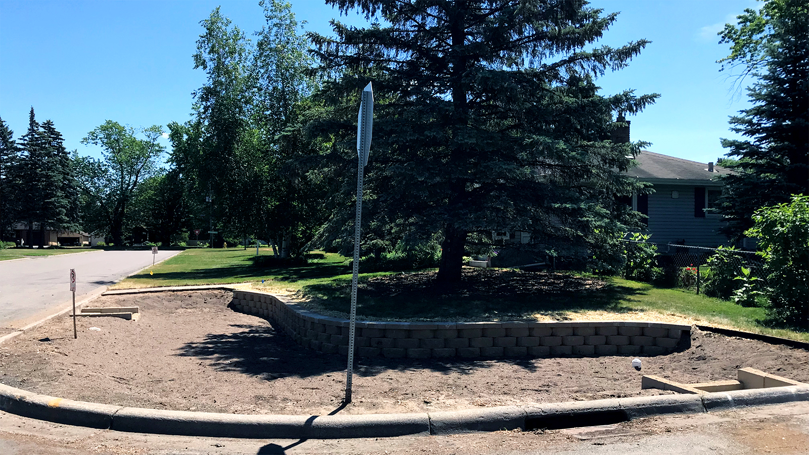 A large dirt basin covers the corner of a residential street. 