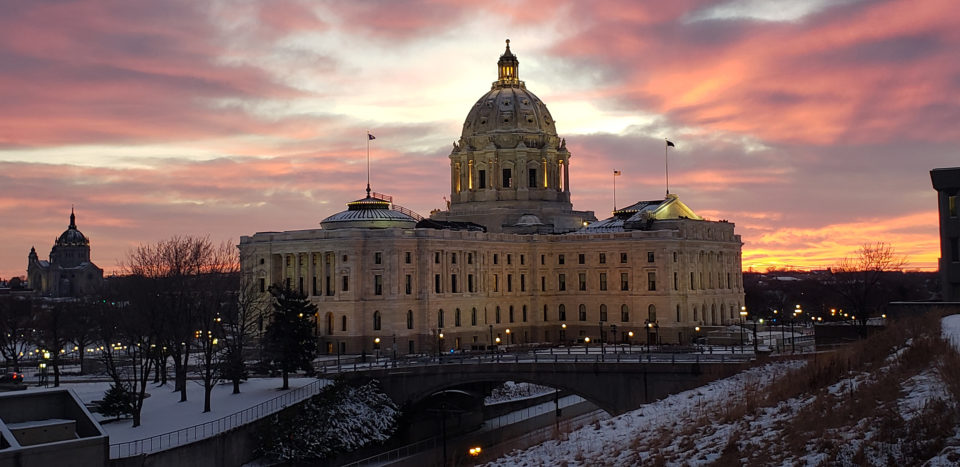 The domed Minnesota State Capitol building with a fading sunset behind it in colors of pink, purple and orange. 