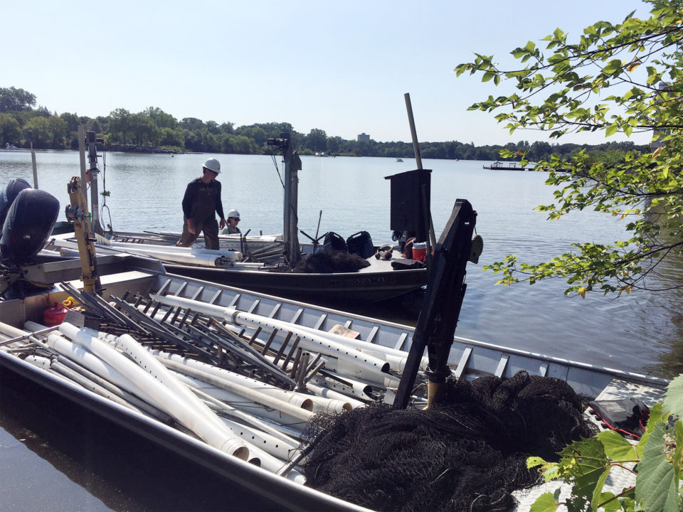 Two motorized boats are loaded with large nets, piping, and polls. 