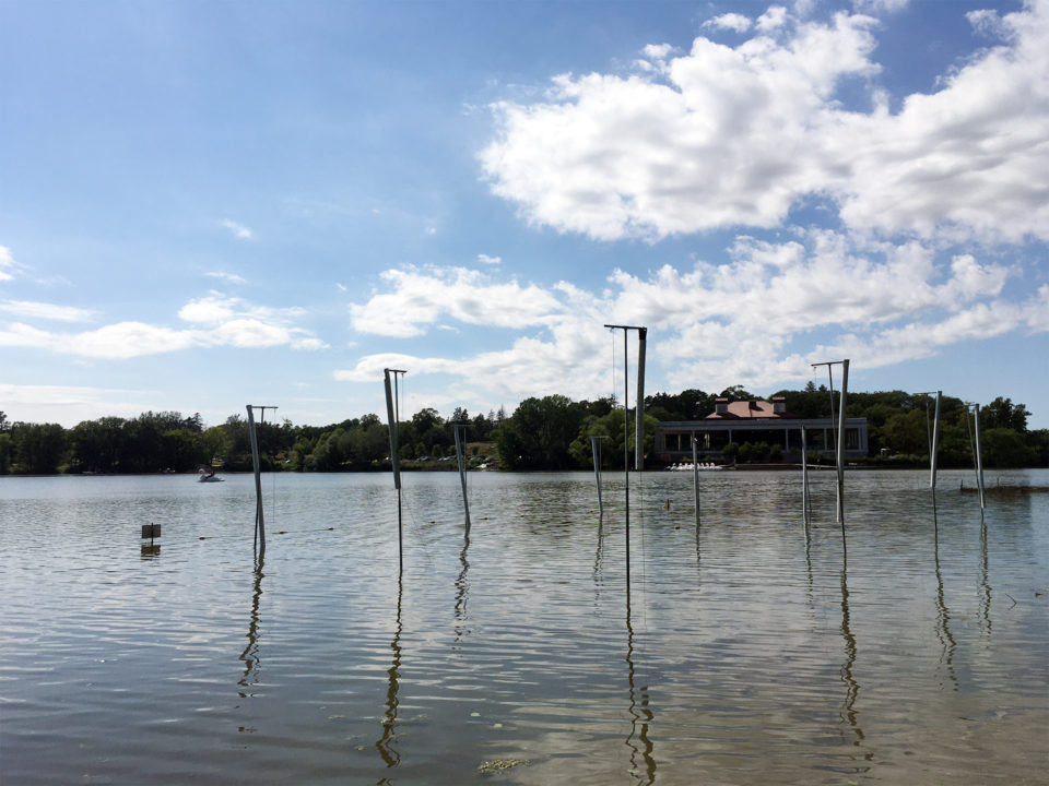Several tall polls in Como Lake reflect off the lake surface in front of Como Lakeside Pavilion. 