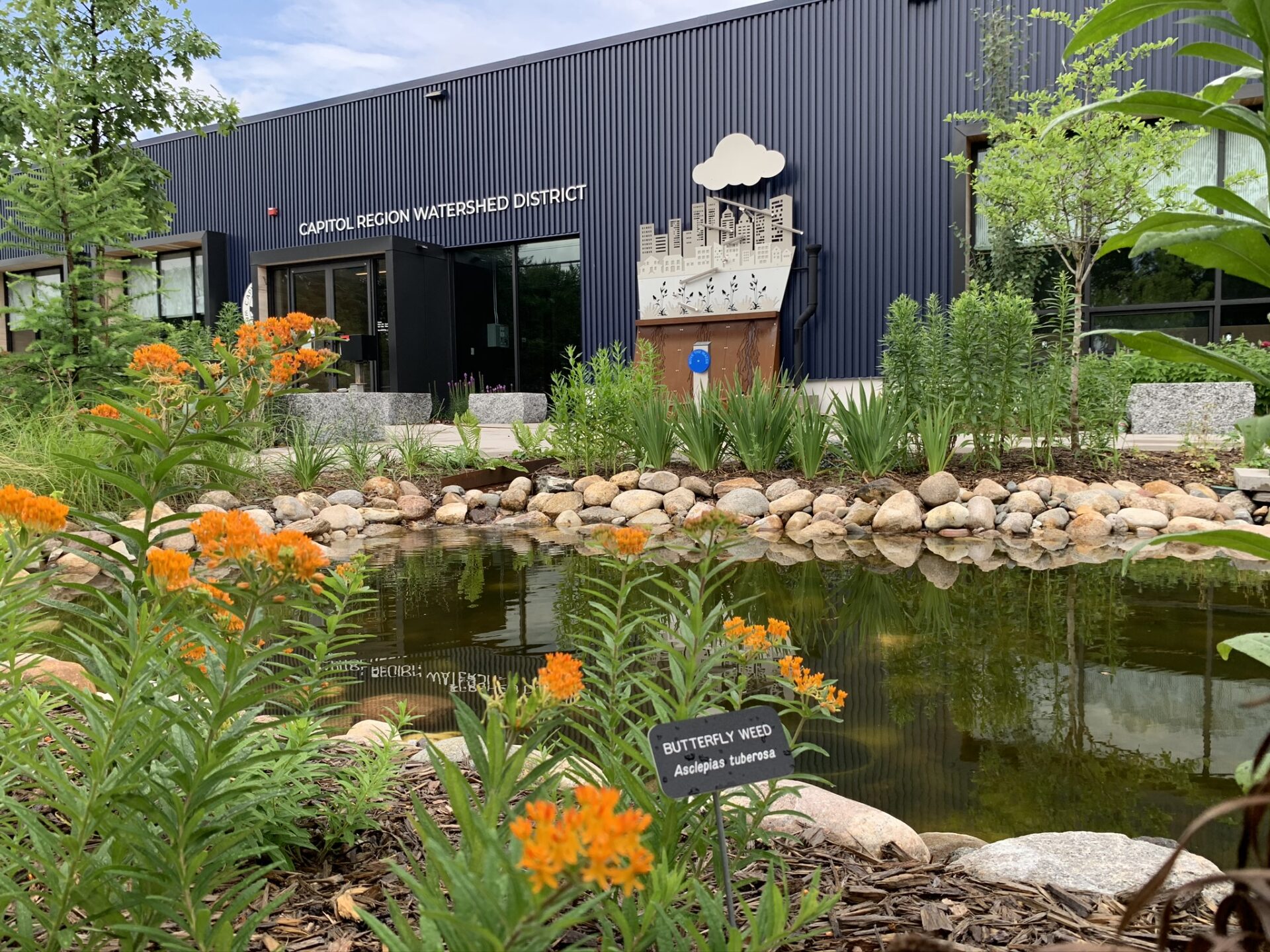 The small, rock-lined pond surrounded by blooming native plants in front of Capitol Region Watershed District's office building.