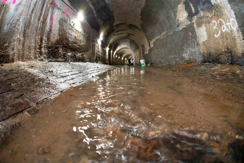 A shallow stream of water running in the bottom of a concrete tunnel. 