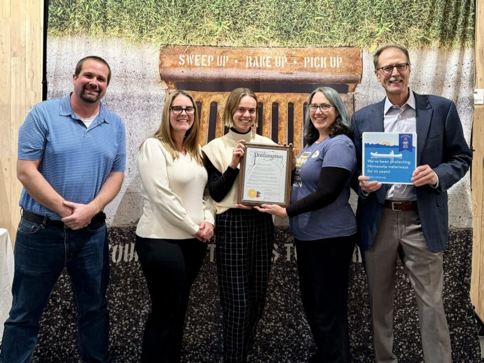 Five people standing in front of a banner with a photo of a storm drain and the text 