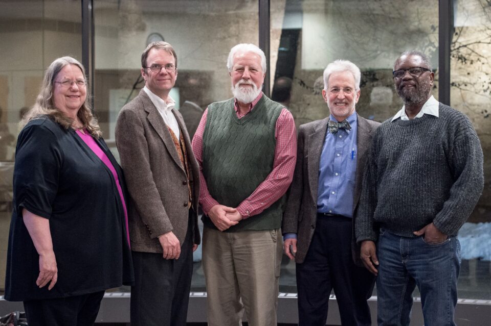 Five smiling people standing in a meeting room.