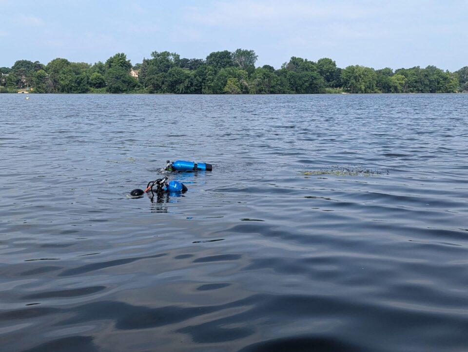 Two SCUBA divers with blue air tanks floating on the surface of Como Lake. 