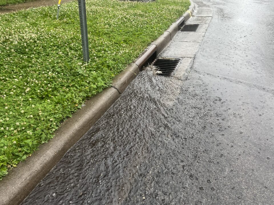 Water flowing along a street curb and into a storm drain during a rainstorm. 