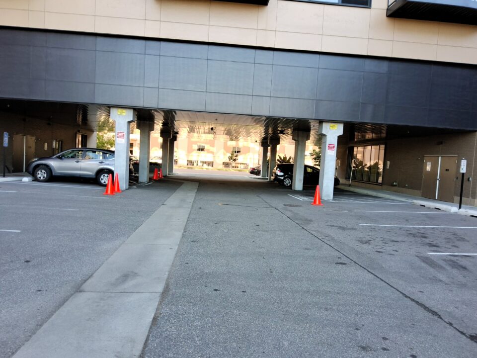 A parking lot with a driveway that passes under a building. The same industrial building is in the background in the photo of the underground filtration system construction. 
