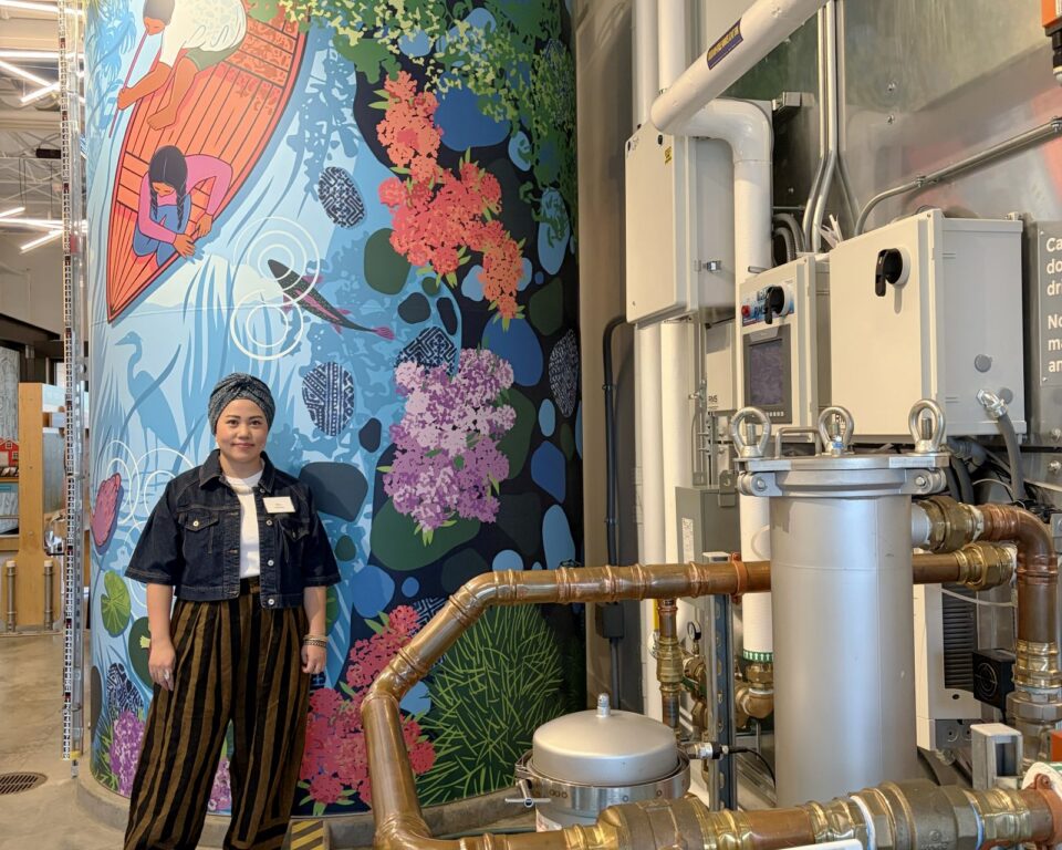 Christina Vang standing in front of a colorful, water-themed mural on a large cistern. 