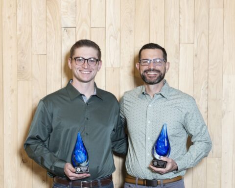 Two people smiling and holding blue-swirled glass raindrop awards.