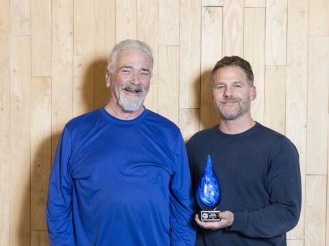 Two people standing, one is holding a blue-swirled glass raindrop award.