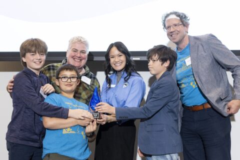 A group of three adults and three children holding a blue-swirled glass raindrop award.