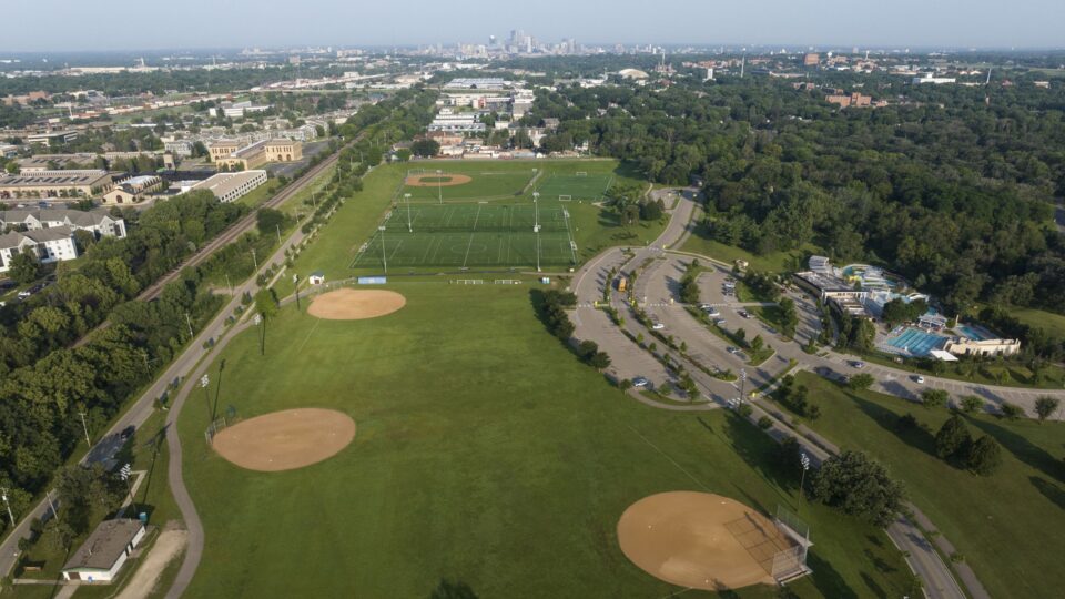 An aerial view of a large park with multiple baseball and soccer fields, an outdoor swimming pool and a large parking lot.
