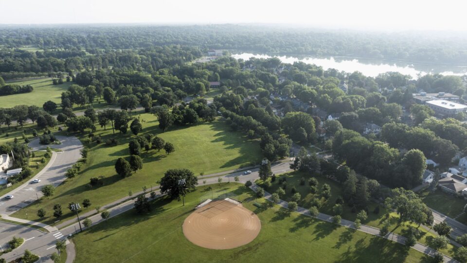 An aerial view of a park with baseball fields and a parking lot, with a lake in the background.