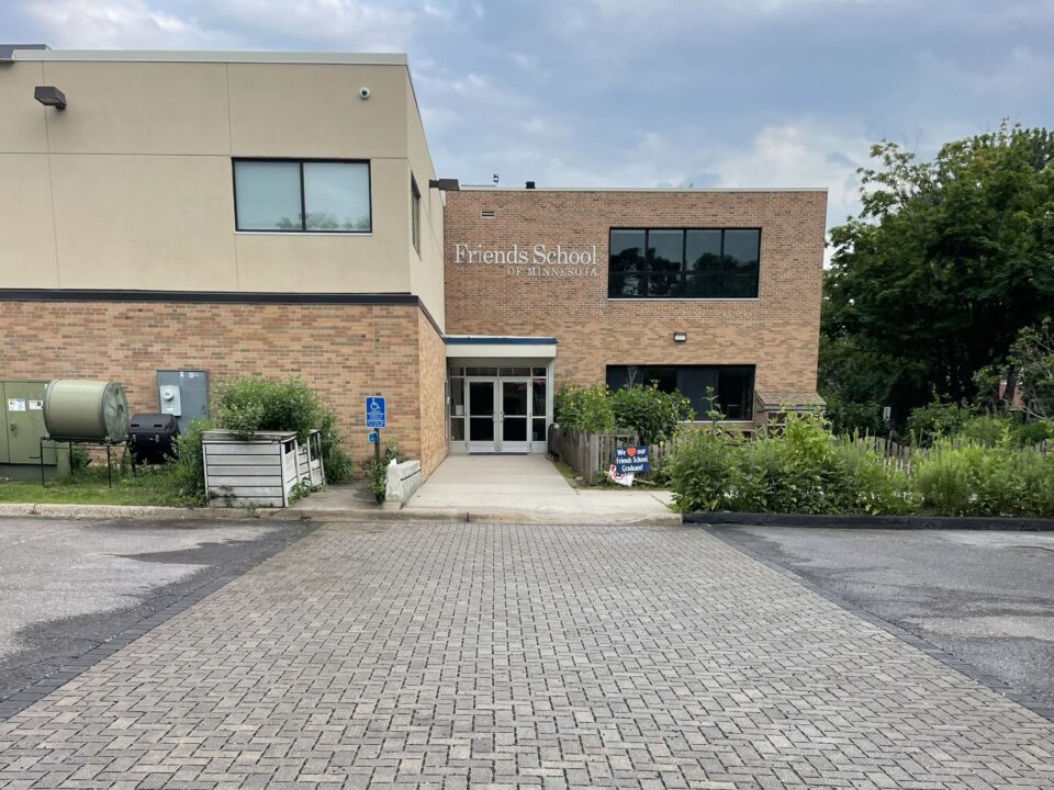 A modern two-story building with “Friends School of Minnesota” over the entrance. A parking lot in front of the building is paved with a section of tidy, gray bricks. 